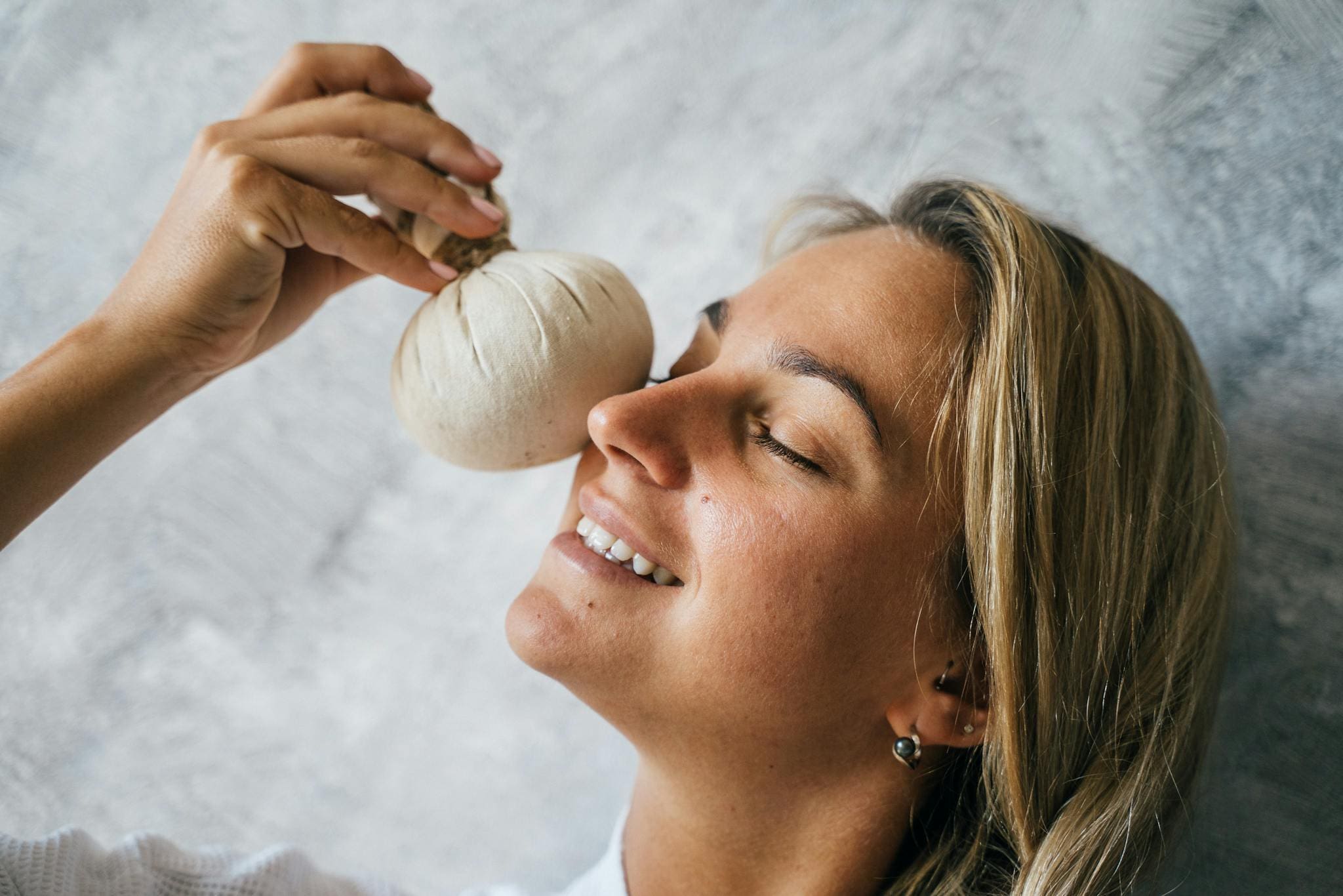A woman enjoying a relaxing herbal facial treatment with a warm pouch, highlighting self-care and wellness.