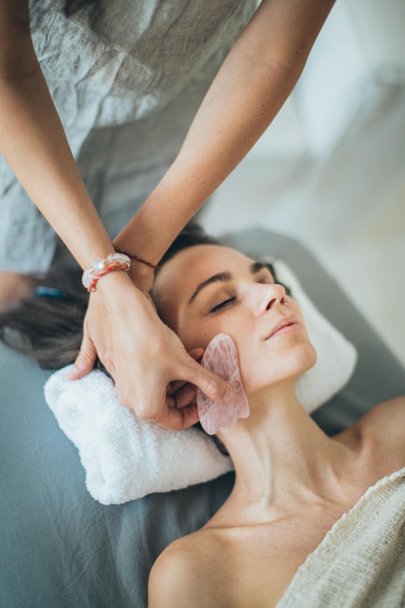 A woman relaxes during a gua sha facial massage at a spa, promoting wellness and beauty.